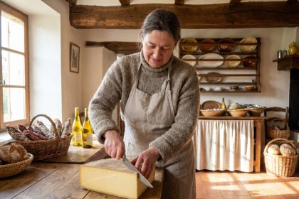 Femme en pull rustique tranche du fromage Comté dans une cuisine chaleureuse