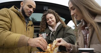 une famille mangeant des pizzas auprès de leur voiture